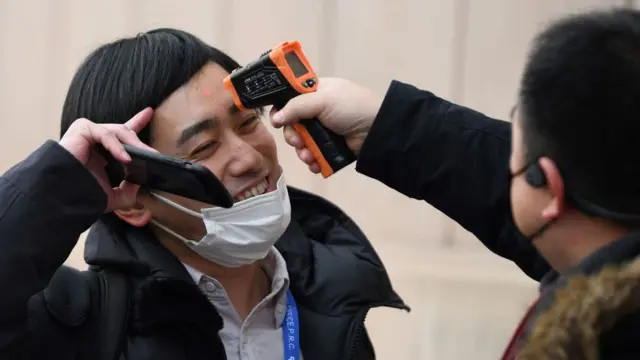 A man smiles as he holds back his fringe for an infra-red thermometer scan