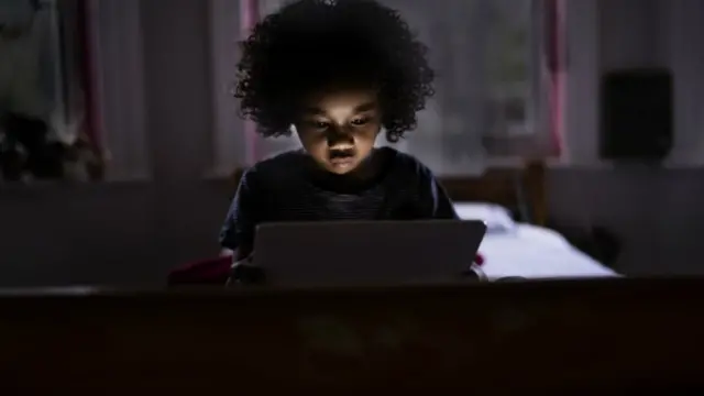 Child surfing internet on a computer tablet in his bedroom