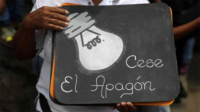 Manifestante con un cartel que dice "Cese el apagón"