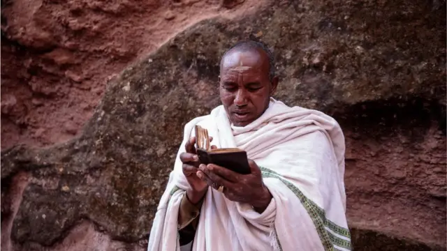 Mutum ya na karanta littafin Injila, sanye da tufafin gargajiya na 'yan kasar Habasha. Ya jingina bayansa jikin wani katon dutse.