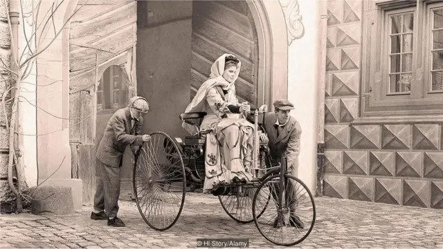 Bertha Benz sobre seu carro, com rodasroleta shopeemadeira