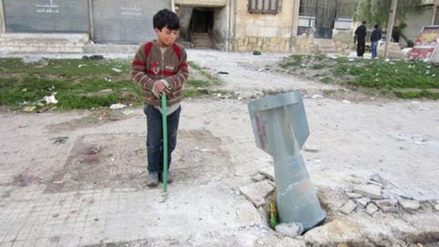 Criança observa bomba de fragmentação na Síria, em 2013