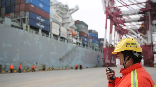 A masked foreman gives orders to other workers serving a container ship upon its arrival in a port in Qingdao in east China's Shandong province Tuesday, Feb. 04, 2020.-