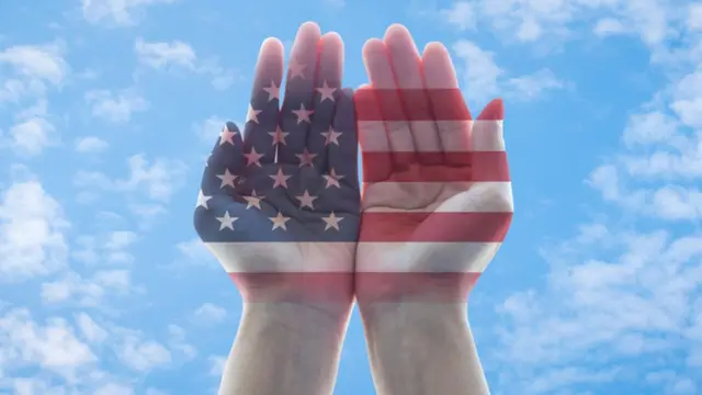 Manos con la bandera estadounidense que apuntan al cielo.