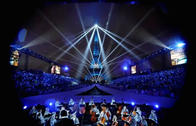 La Tour Eiffel est illuminée de lumières et de lasers et le signe olympique avec un orchestre au premier plan, lors de la cérémonie d'ouverture des Jeux olympiques de Paris 2024.
