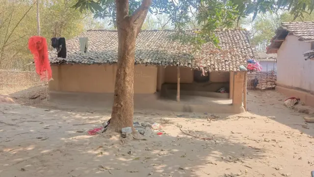 Скромний дім жертви серед дерев, а на задньому плані — звичайний одяг.