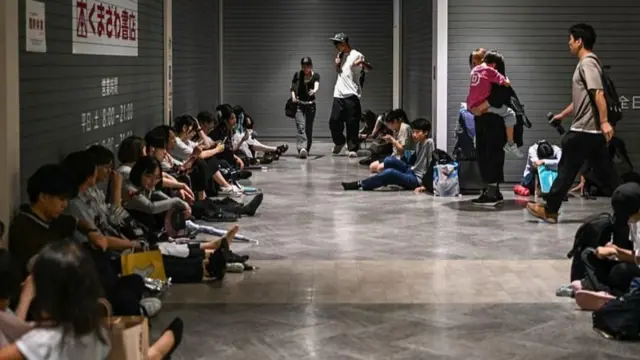 ショッピングモールの床に座り、店舗の灰色のシャッターによりかかる人たち