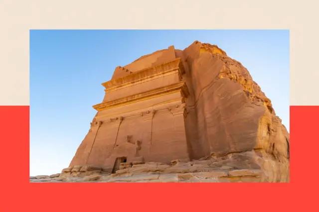 A large yellow rock monument looms against a bright blue sky