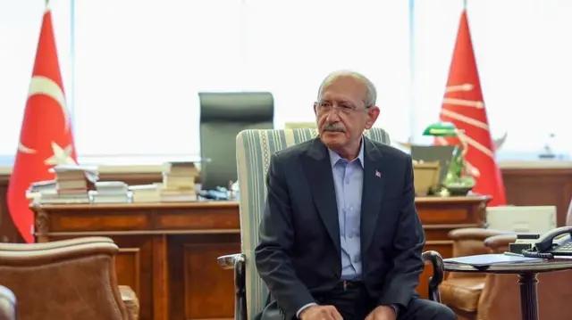 Kemal Kılıçdaroğlu iki yanında CHP ve Türk bayrağı olan bir masanın önündeki koltuğunda oturuyor