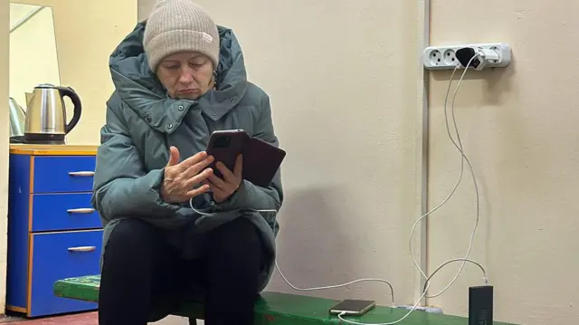 Жінка у синій куртці заряджає гаджети у пункті незламності