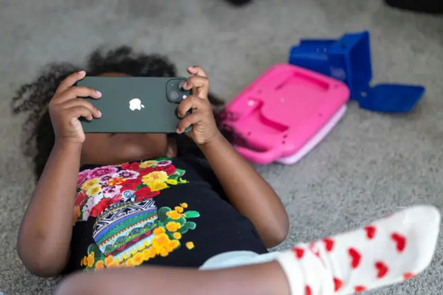 Uma criança deitada com o celular na mão