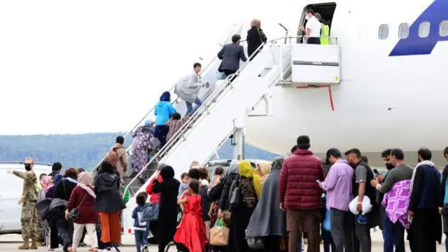 تصویر شماری از پناه‌جویان افغان در یکی از میدان‌های هوایی آلمان. این پناه‌جویان در صف ایستاده اند تا سوار هواپیما شوند.