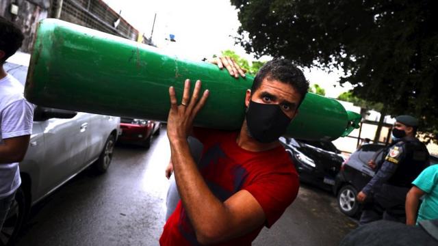 Um homem carrega um cilindro de oxigênio enquanto pessoas fazem fila para comprá-lo de vendedores particulares para tratar de parentes doentes em Manaus, 15 de janeiro de 2021