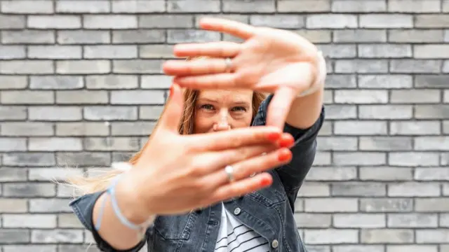 Close-up of woman against grey brick wall making finger frame sign