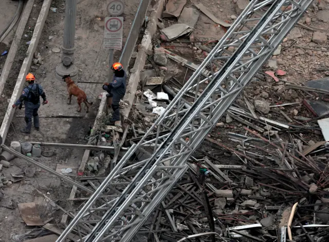 Bombeiros e cão farejador nos escombros do prédio