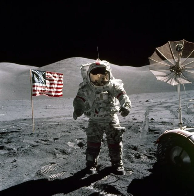 Astronauta da Apollo 17sites de apostas que dão bônuspé sobre a superfície lunar com a bandeira dos Estados Unidos e uma antena parabólica ao fundo