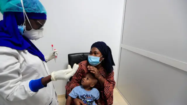 Une femme et son fils avec un agent de santé couvert d'un équipement de protection afin de prélever leurs échantillons pour le depistage du COVID-19) dans un centre de test de l'Institut de recherche en santé, de surveillance épidémiologique et de formation (IRESSEF), à Dakar , Sénégal 24 juillet 2020