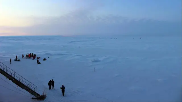 北极星号上的科学家使用研究器材在冰上工作，一位谨防北极熊来袭的观察者正在搜寻远在天边的北极熊的出没。