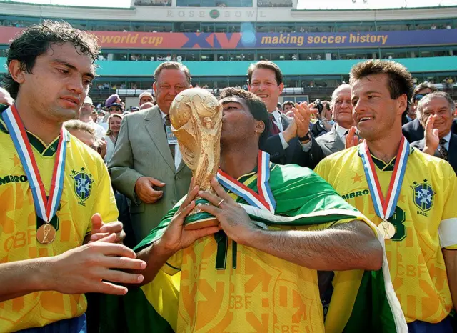 L'attaquant brésilien Romario embrasse le trophée de la Coupe du Monde de la FIFA sous le regard de ses coéquipiers Branco (à gauche) et Dunga, après la victoire du Brésil face à l'Italie (3-2 aux tirs au but, 0-0 après prolongation) en finale de la Coupe du Monde, le 17 juillet 1994 au Rose Bowl de Pasadena. 