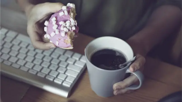 Teclado e duas mãos segurando uma rosca doce e um café