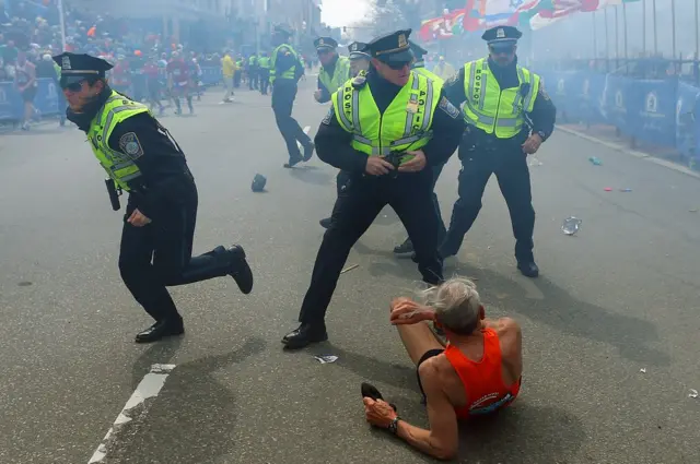 Police officers with their guns drawn hear the second explosion down the street. The first explosion knocked down 78-year-old US marathon runner Bill Iffrig at the finish line of the 117th Boston Marathon.