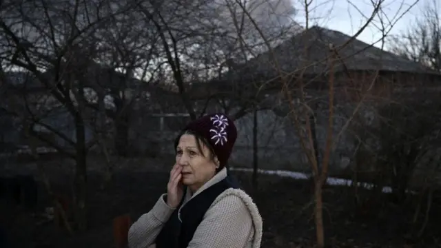 கார்கிவ் அருகேயுள்ள சுகுயேவின் இராணுவ விமான நிலையத்தில் இருந்து எழும்பும் கருப்புப் புகையை வேதனையோடு பார்க்கும் பெண்