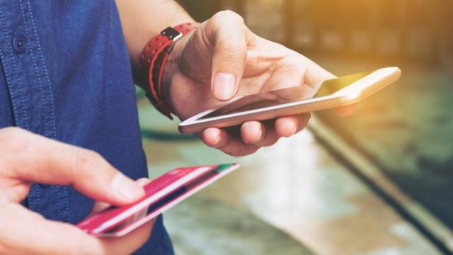 Pessoa com celular e cartão nas mãos