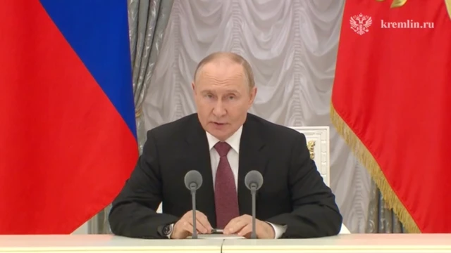 Путін перед мікрофонами на тлі прапорів Росії