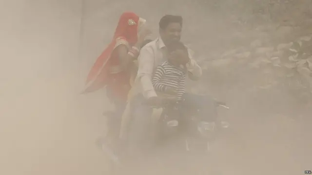 An Indian man and his family ride a bike during heavy dust and smog in New Delhi
