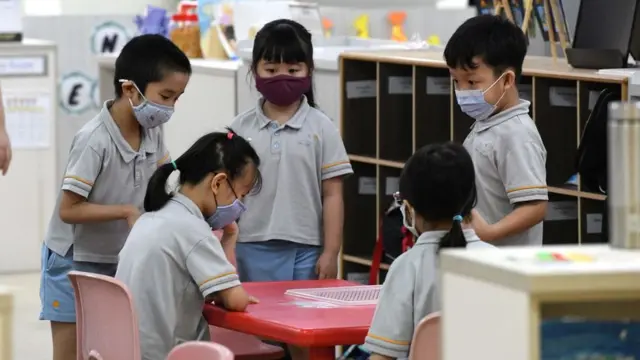 Children wearing face masks gather around a table inside their classroom in Singapore