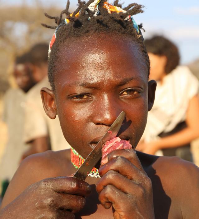 Criança hadza comendo carne vermelha