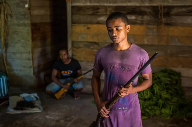 Imagem mostra dois homens armados nas proximidadesbetmotion predictionvagensbetmotion predictionbaunilha armazenadas no chãobetmotion predictionuma casa. Agricultores têm se armado para proteger a safrabetmotion predictionladrões