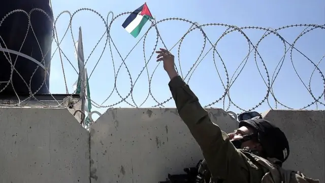 Soldado israelí retira una bandera palestina del muro en Cisjordania