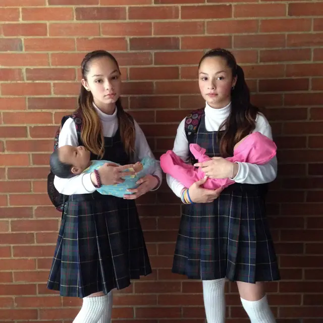 Gemelas de 12 años con bebés de juguete en los brazos.