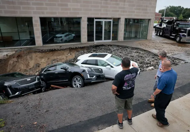 Leominster, MA - September 12: People gather to look at a sinkhole that swallowed vehicles at a Cadillac dealership following massive flooding. (Photo by Jessica Rinaldi/The Boston Globe via Getty Images)