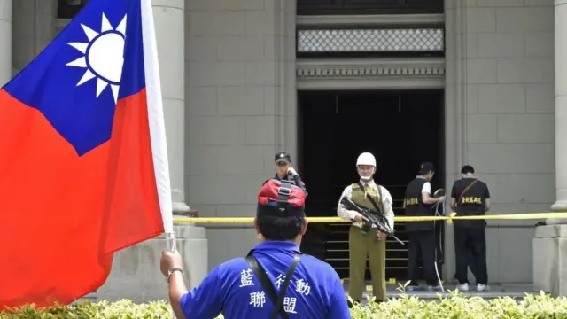 Un manifestante com uma bandeiraaposta menos 1.5Taiwanaposta menos 1.5frente a um edifício oficial en Taipei