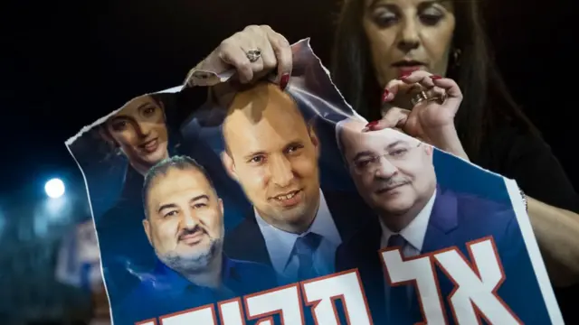امرأة إسرائيلية تمزق ملصقا لنفتالي بينيت ومنصور عباس وأحمد الطيبي