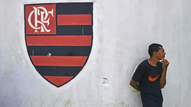 Homem ao lado de escudo do Flamengo pintado; incêndio em centro de treinamento deixou dez mortos