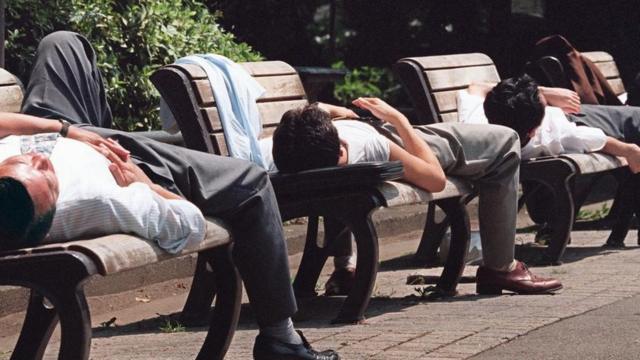 Hombres japoneses durmiendo una siesta en las sillas de un parque