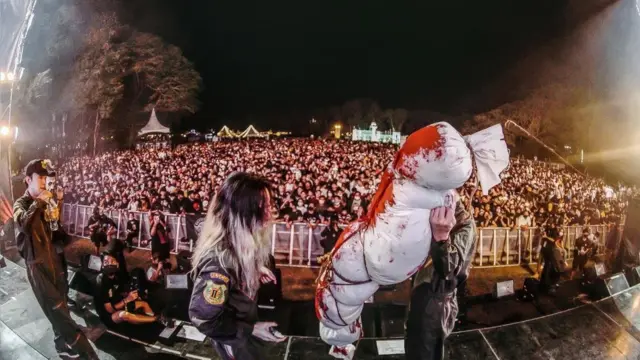กลุ่มศิลปินวง Sweet Mullet แต่ตัวในชุดอาสากู้ชีพและแบกมัดผ้าสีขาวมีรอยคล้ายคราบเลือดขึ้นเวที