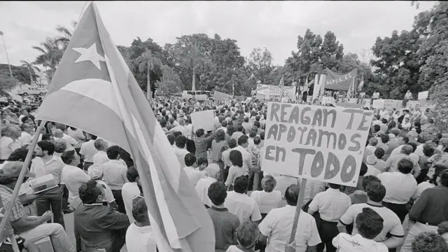 A bandeira cubana ao ladojogos de apostaum cartaz que diz,jogos de apostaespanhol, 'Reagan, te apoiamosjogos de apostatudo' durante uma manifestaçãojogos de aposta1983