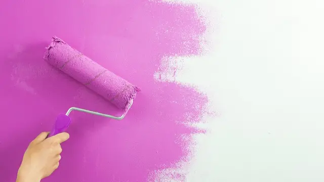 Рука красит белую стену в розовый цвет