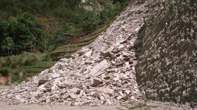 Pile of rocks and debris from a landslide next to a steep, rocky hillside.