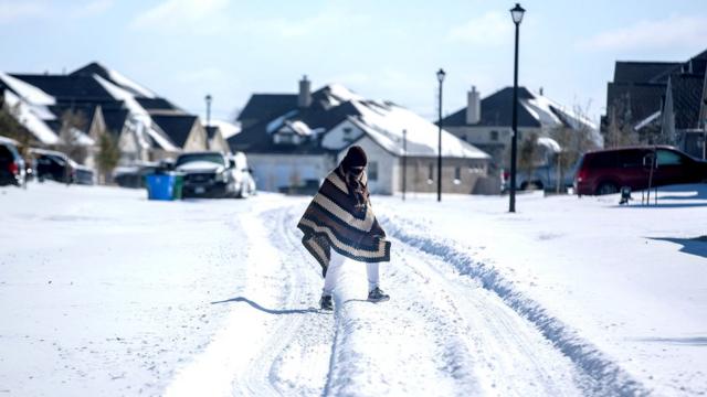 رجل يسير إلى منزل صديقه في حي بدون كهرباء بينما يغطي الثلج حي بلاك هوك في بفلوغرفيل، تكساس، 15 فبراير/شباط 2021