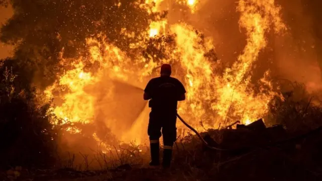 A firefighter tries to extinguish a wildfire burning in the village of Pefki