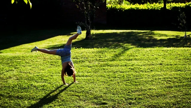 یک کودک روی چمن در حال حرکت ژیمناستیک چرخ فلک