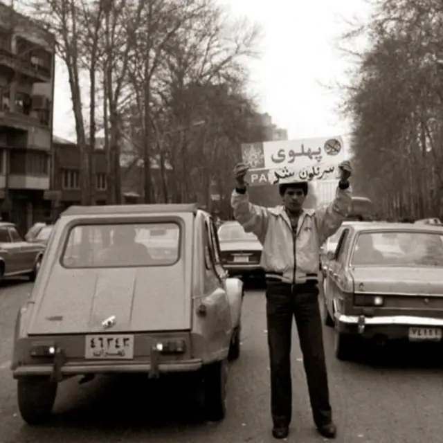 مردی که پلاک خیابان پهلوی را دست دارد که بر روی آن نوشته شده پهلوی سرنگون شد