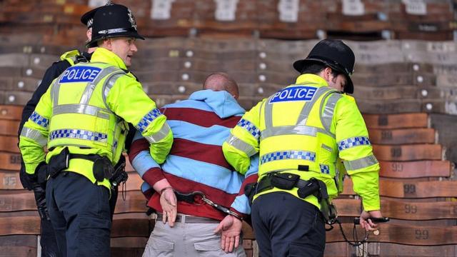 A fan is led away in hand cuffs by police after a scuffle in the crowd after the English Premier League football match