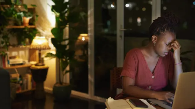 Une jeune femme à l'air stressé qui travaille sur un ordinateur portable chez elle, la nuit.