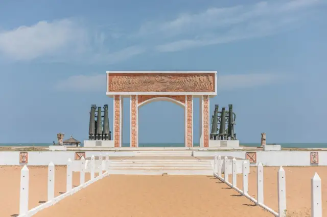 Grande monumento, em formato de portal, com mar ao fundo